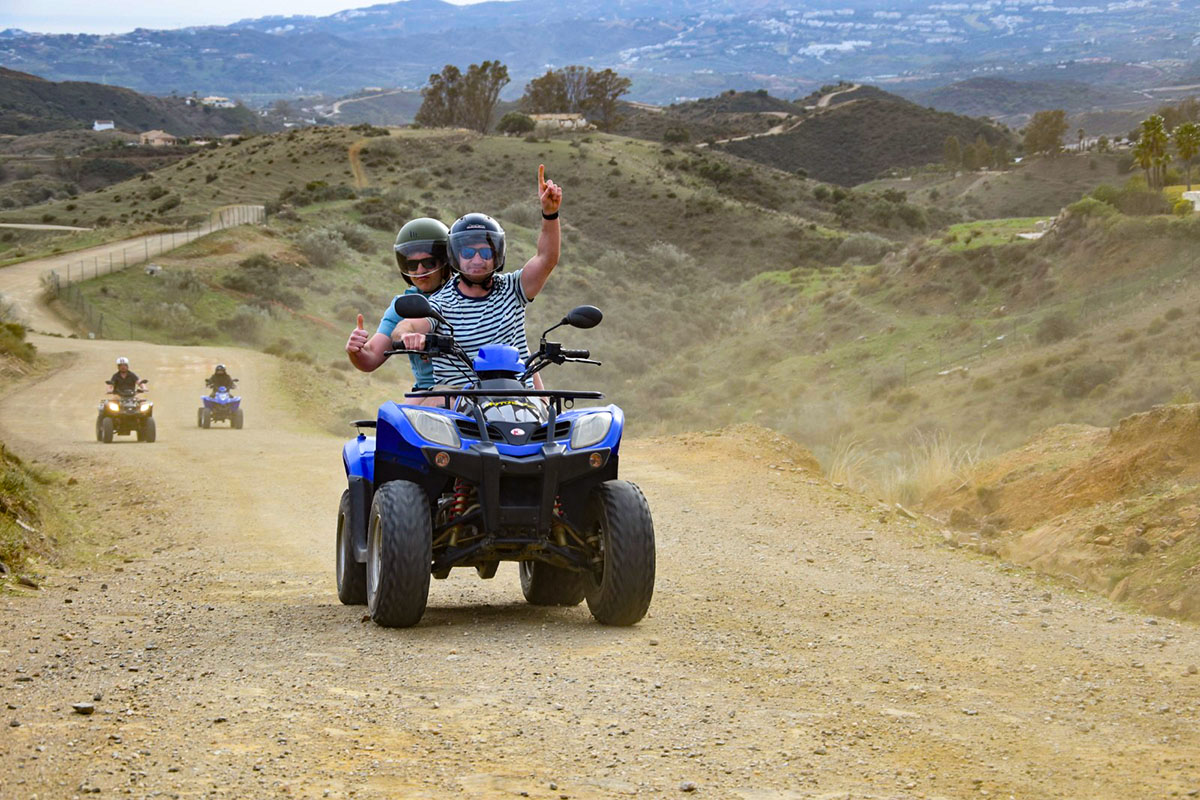 quad riders riding uphill and holding thumbs up smiling