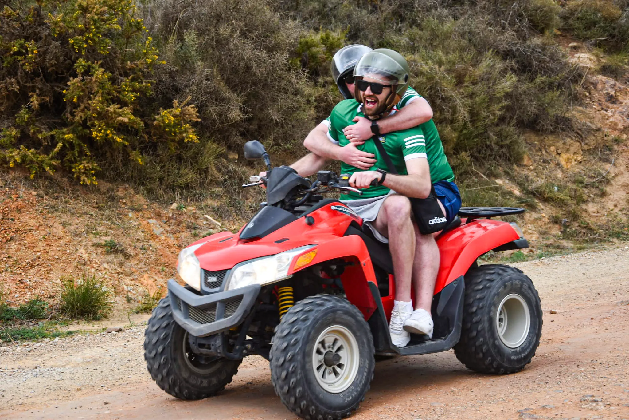 two quad riders laughing and hugging as they ride a quad